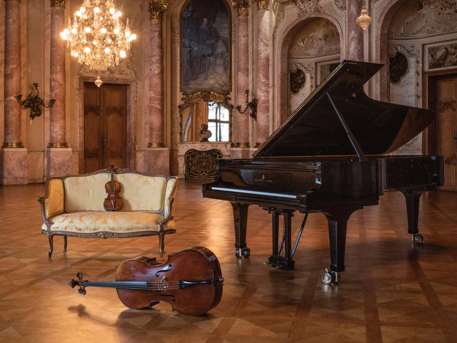 Blick in den Bückeburger Schlosssaal mit drapierten Musikinstrumenten: Cello, Violine und Klavierflügel